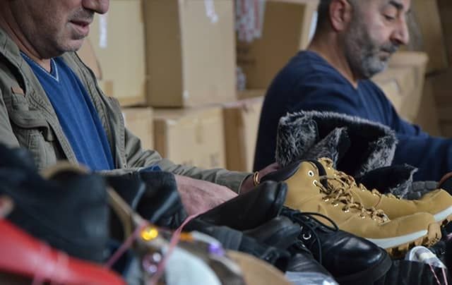 A man hand sorts shoes with a mountain of cardboard boxes in the background